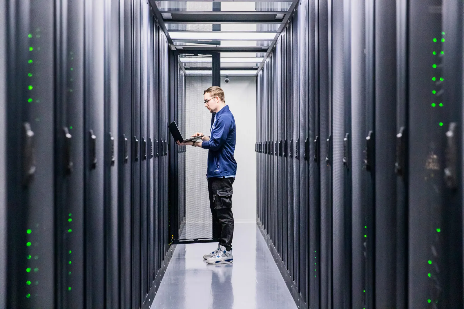 Jongen met een bril die bezig is met zijn laptop in het datacenter